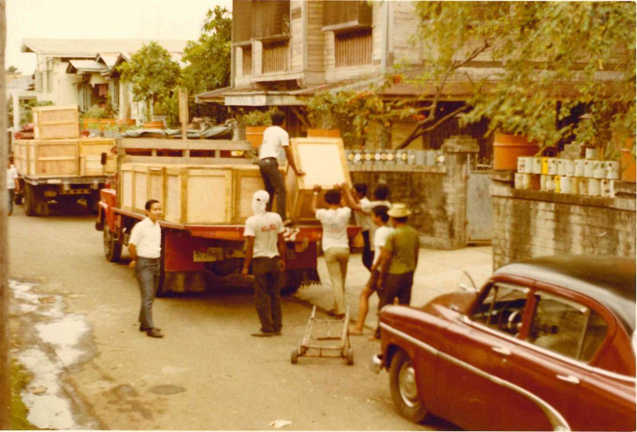 Sepia photo of a group of men unloading boxes from a truck on he side of the street